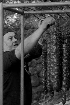 Black and white photo of a man preparing Cevizli Sucuk outdoors in Erzincan, Turkey.