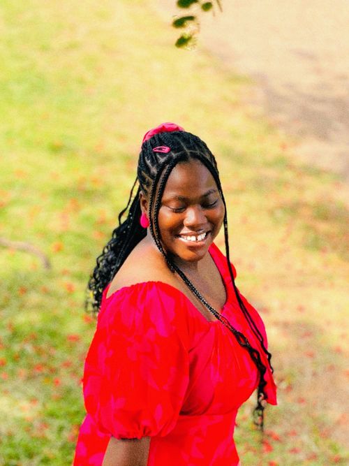 Free A woman in a vibrant red dress smiles outdoors during a sunny day. Stock Photo