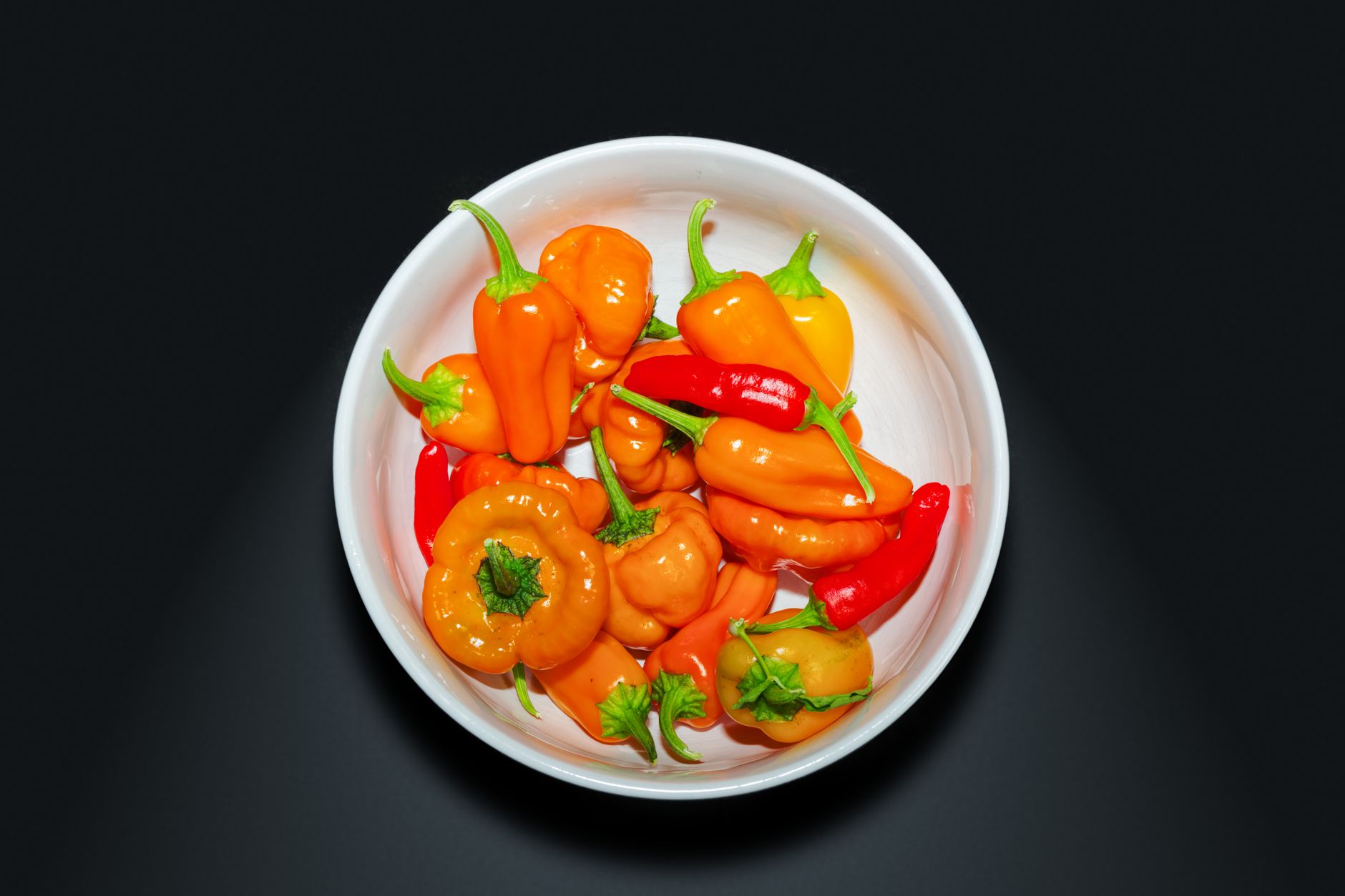 Bowl of golden ají amarillo paste surrounded by fresh rocoto and ají panca peppers on rustic wooden surface