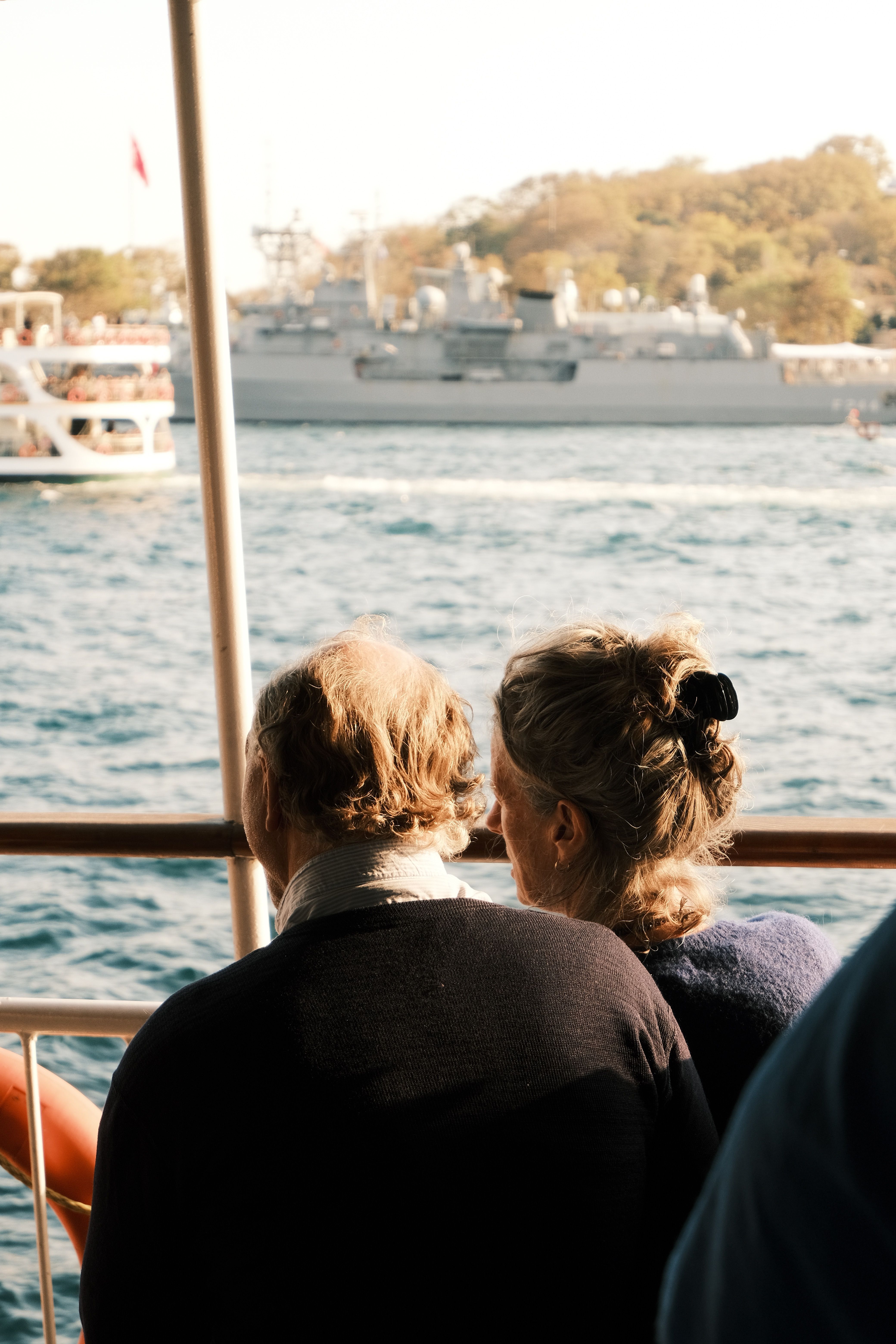 A senior couple gazing at the sea from a boat with ships in the background, capturing a serene moment.
