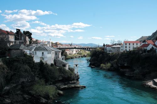 Free Breathtaking view of Mostar's Neretva River with picturesque houses and bridge on a sunny day. Stock Photo