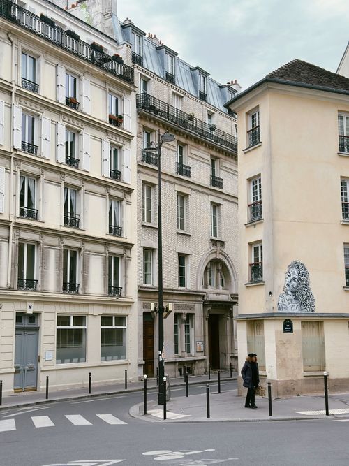 Free Quaint Parisian street scene featuring classic architecture and a lone pedestrian on a quiet corner. Stock Photo