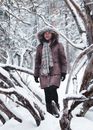 一位女士身着冬季外套和围巾，在白雪皑皑的森林中摆姿势，展示冬季时尚风格