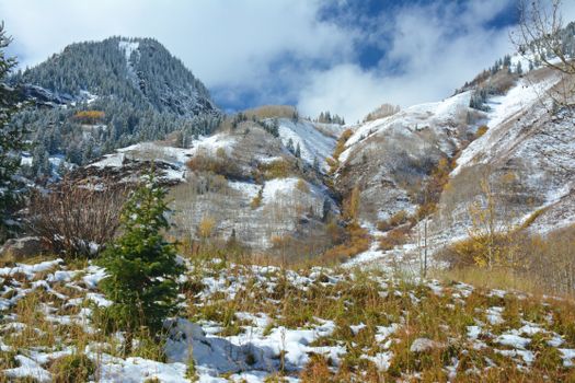 Scenic view of Aspen, Colorado mountains with fresh autumn snow under a partly cloudy sky.