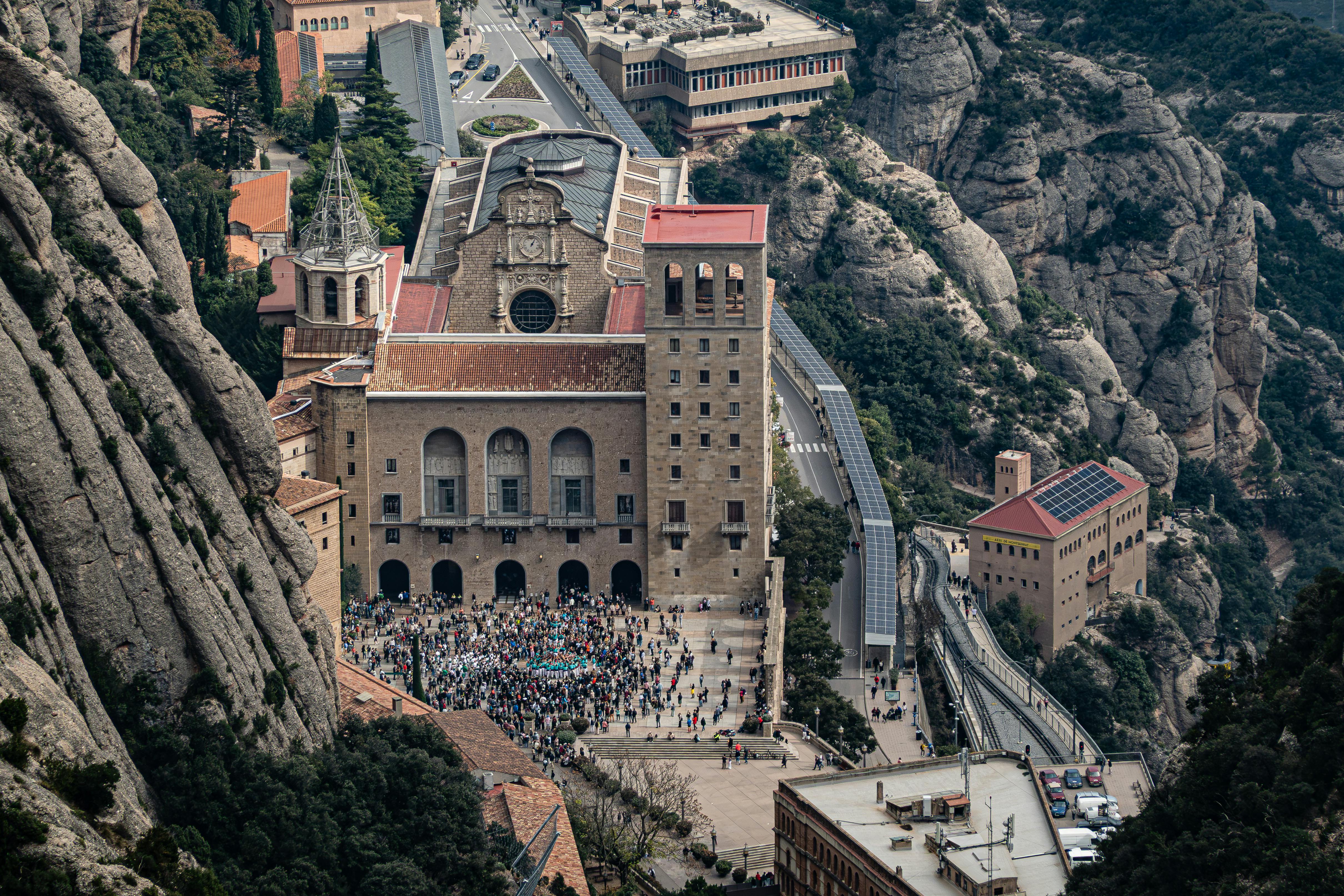 Aerial shot of Santa Maria de Montserrat Abbey nestled in rocky mountains with tourists visiting.