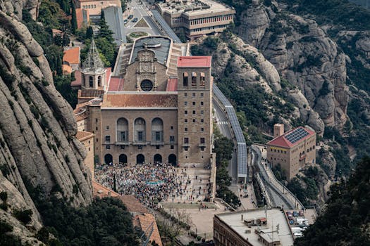 Aerial shot of Santa Maria de Montserrat Abbey nestled in rocky mountains with tourists visiting.