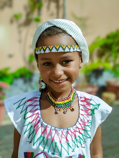 Free A young girl wearing a vibrant traditional outfit smiles outdoors on a sunny day. Stock Photo