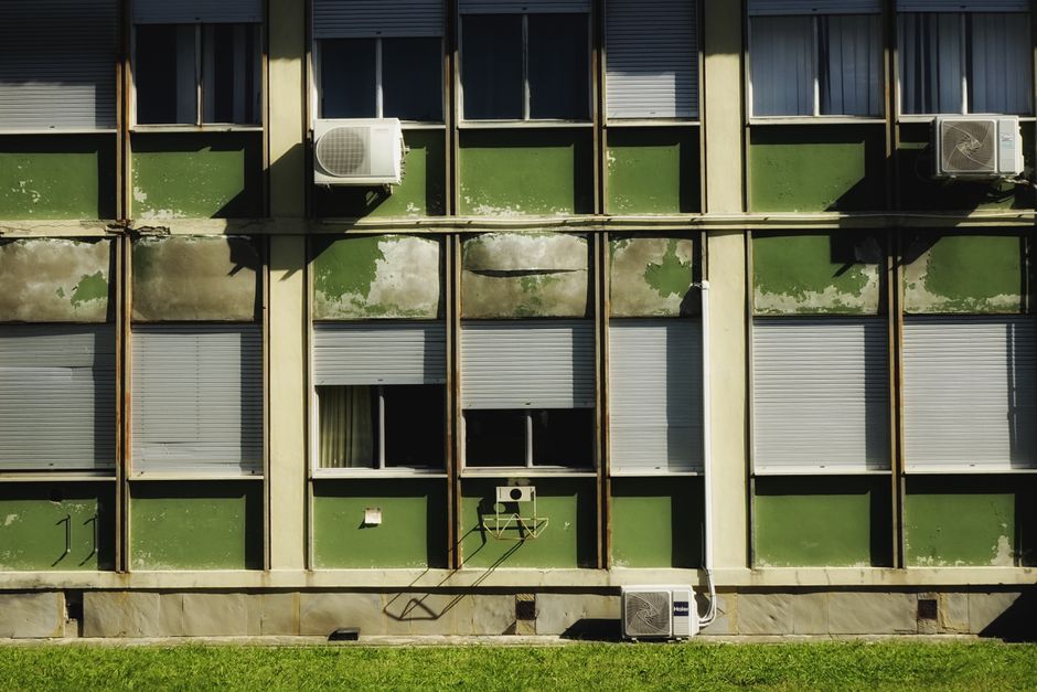 Close-up of an old building facade with air conditioners and green paint, showing urban decay.