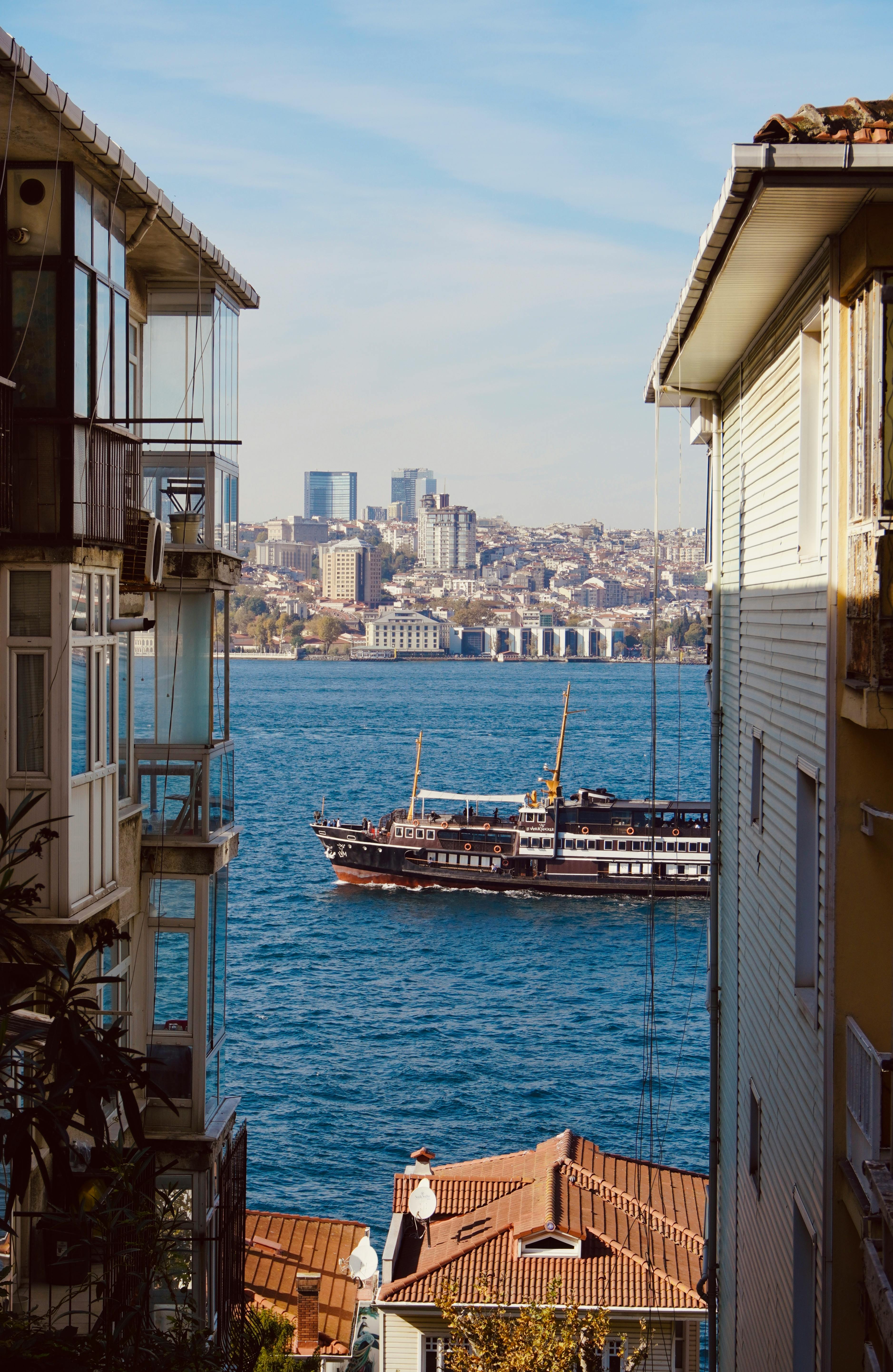 Ship sailing on Bosphorus Strait framed by buildings in Istanbul, under a clear sky.