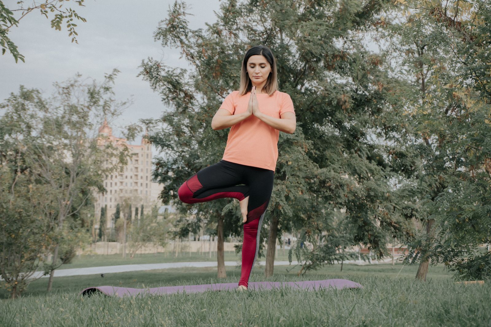 Woman practicing tree pose outdoors in a park with trees in the background