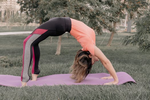 A woman performing the downward dog pose on a yoga mat in a grassy park setting.