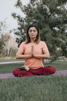 Peaceful woman practicing yoga in a serene park setting, meditating with closed eyes.