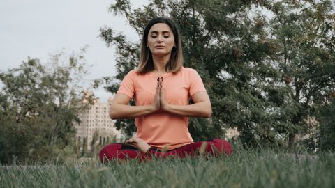 Woman practicing yoga and meditation in park. Enhancing mindfulness and relaxation outdoors.
