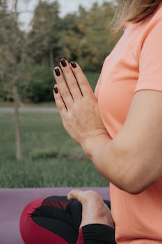 A close-up of a person meditating outdoors in a peaceful yoga pose with hands in prayer position.