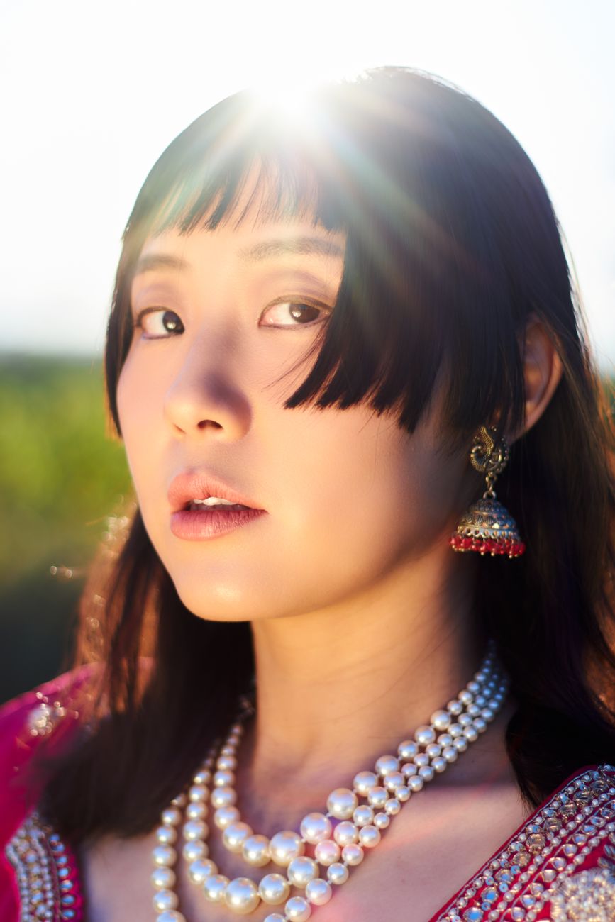 A woman in traditional attire with pearls and earrings, sunlit outdoors in Toronto.