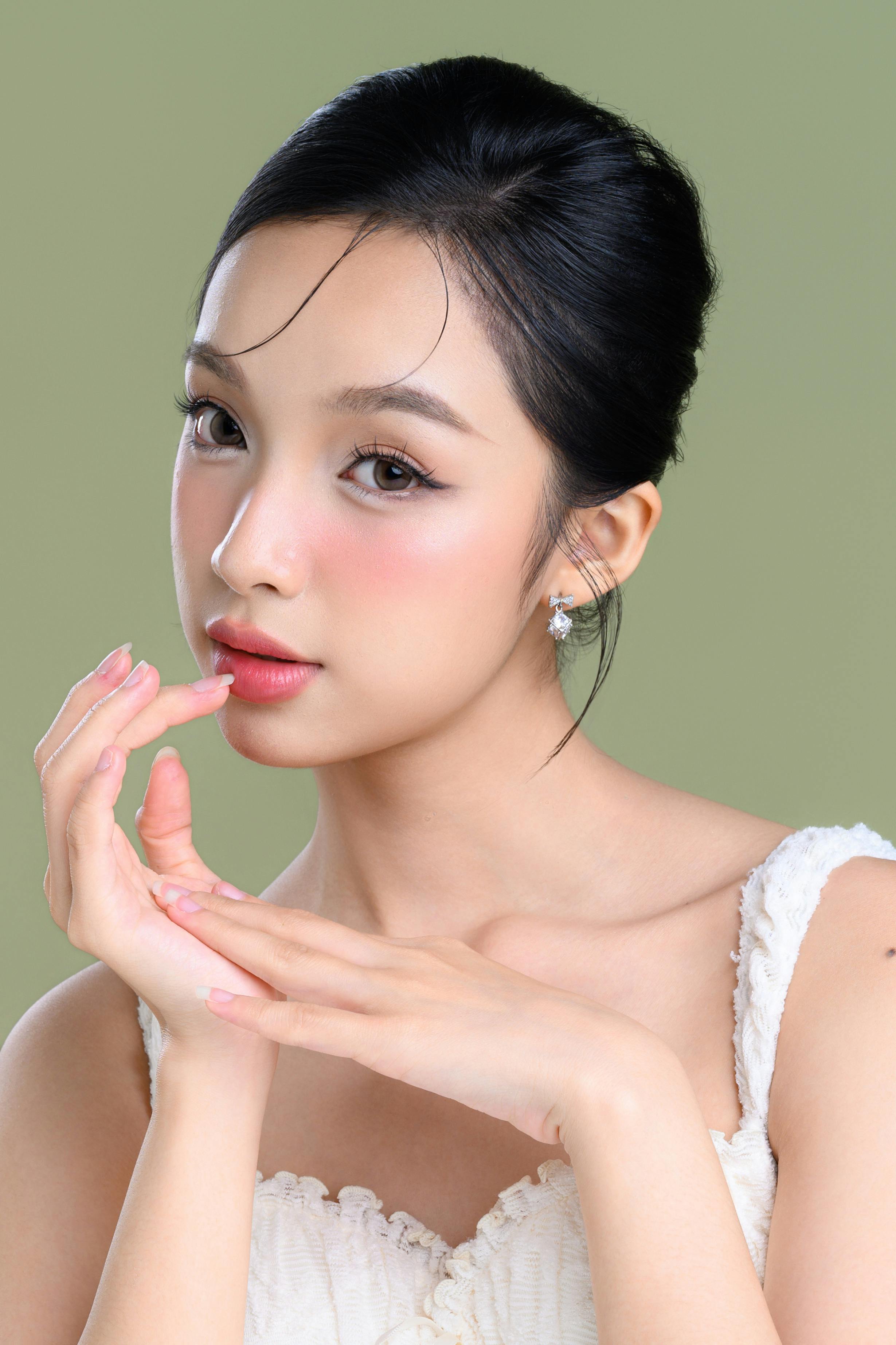 Elegant portrait of a young woman with styled hair and makeup against a green backdrop.