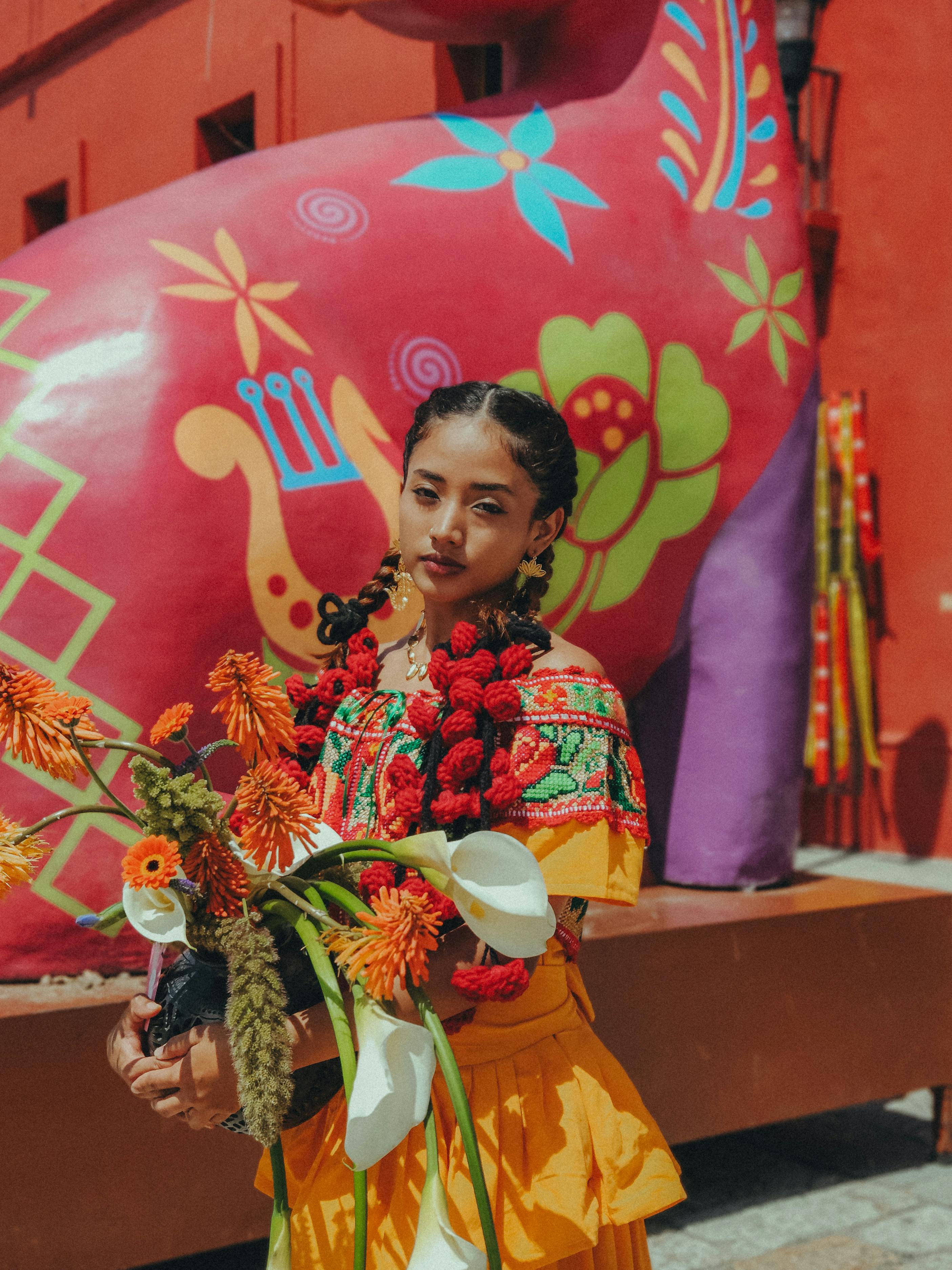 Free Young woman in traditional Oaxacan dress holding flowers against a vibrant backdrop in Mexico. Stock Photo
