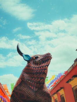 Vibrant art and cultural expression in Oaxaca, featuring a decorated bull sculpture and colorful banners under a blue sky.