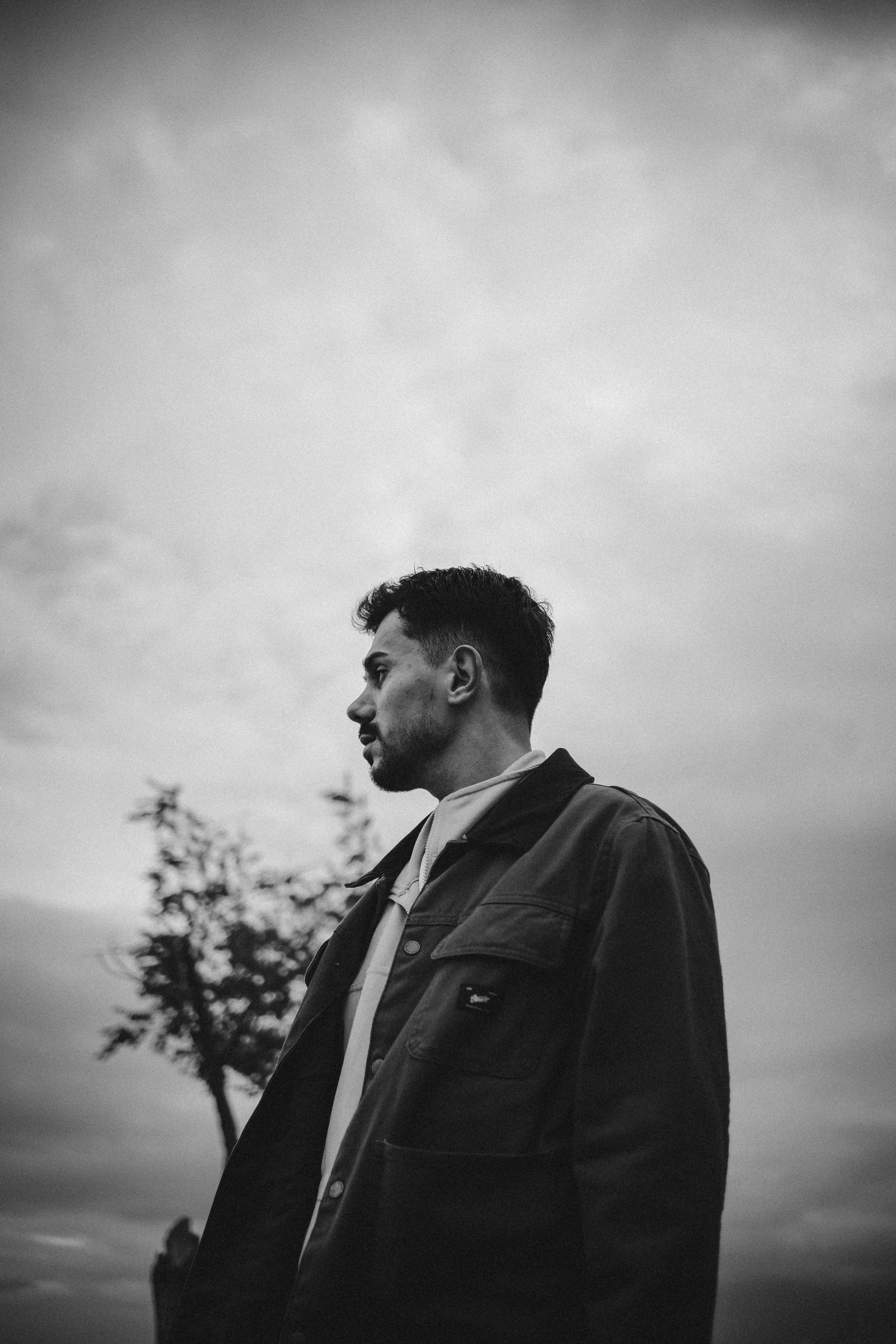 A side-profile black and white portrait of a man standing outdoors with a moody sky.