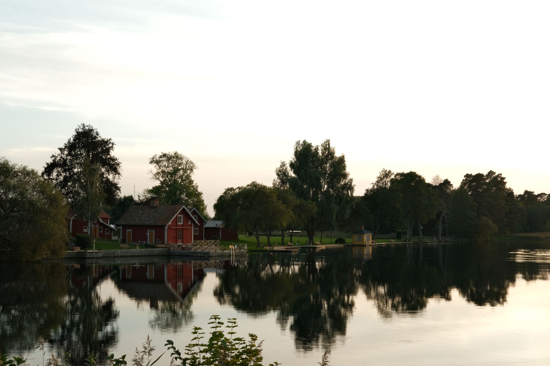 Idyllic lakeside view of red houses and trees reflected on calm water.