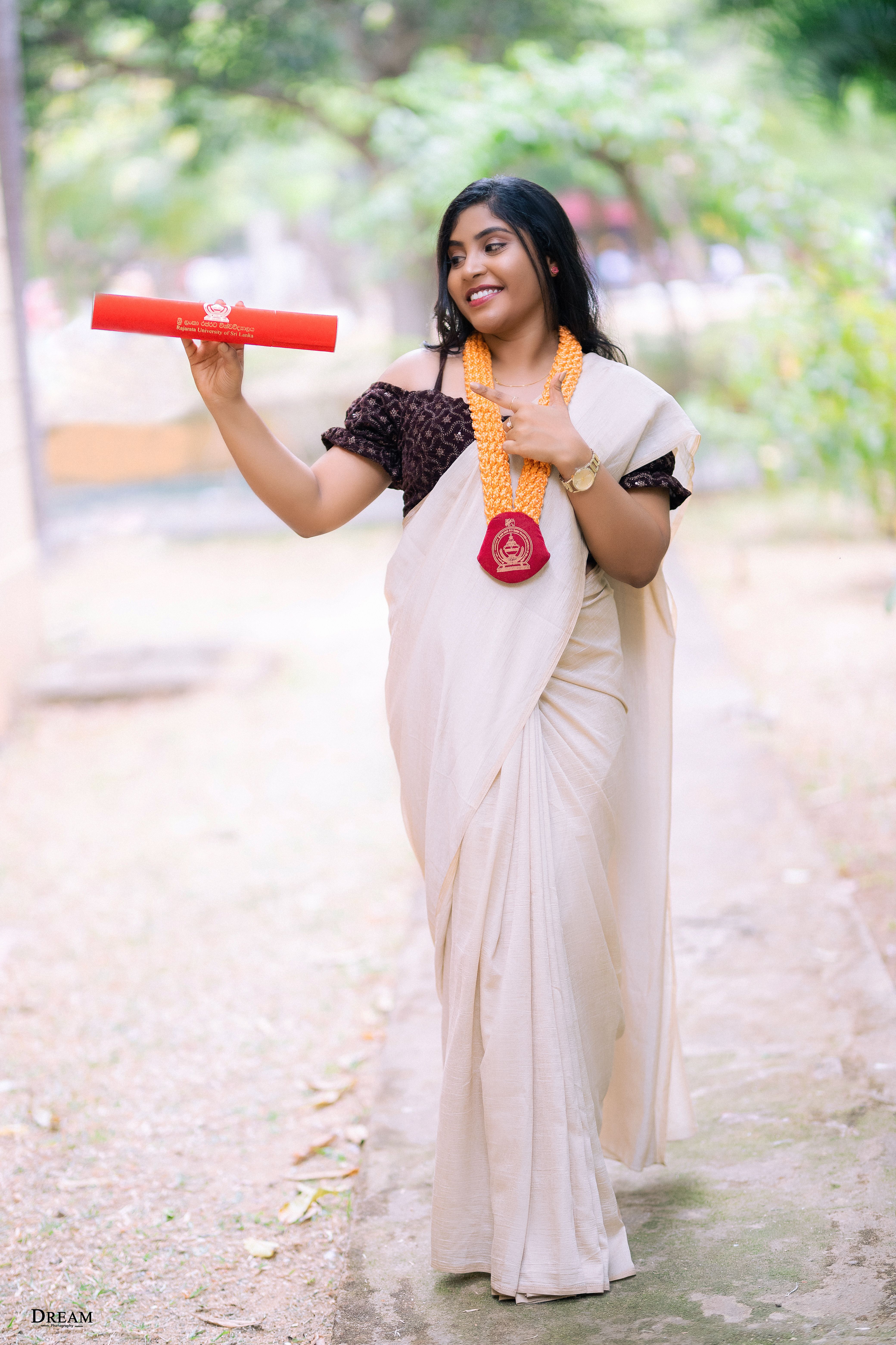 Happy graduate in traditional attire with diploma outdoors in Mihintale, Sri Lanka.