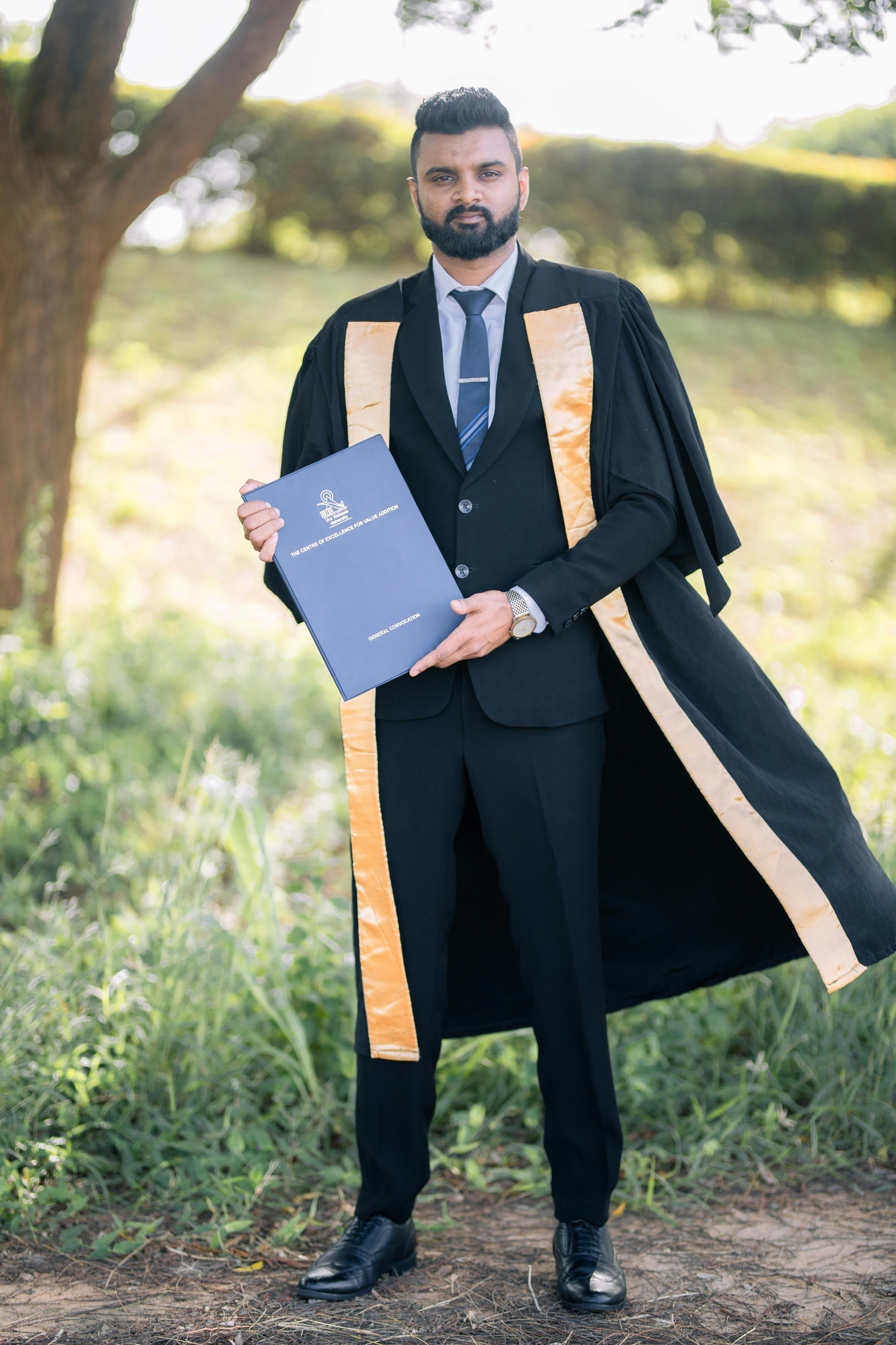 A proud graduate holding a diploma in an outdoor ceremony in Hambantota, Sri Lanka.