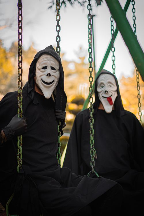 Free Two individuals in masks and black cloaks sitting on swings in a park. Stock Photo