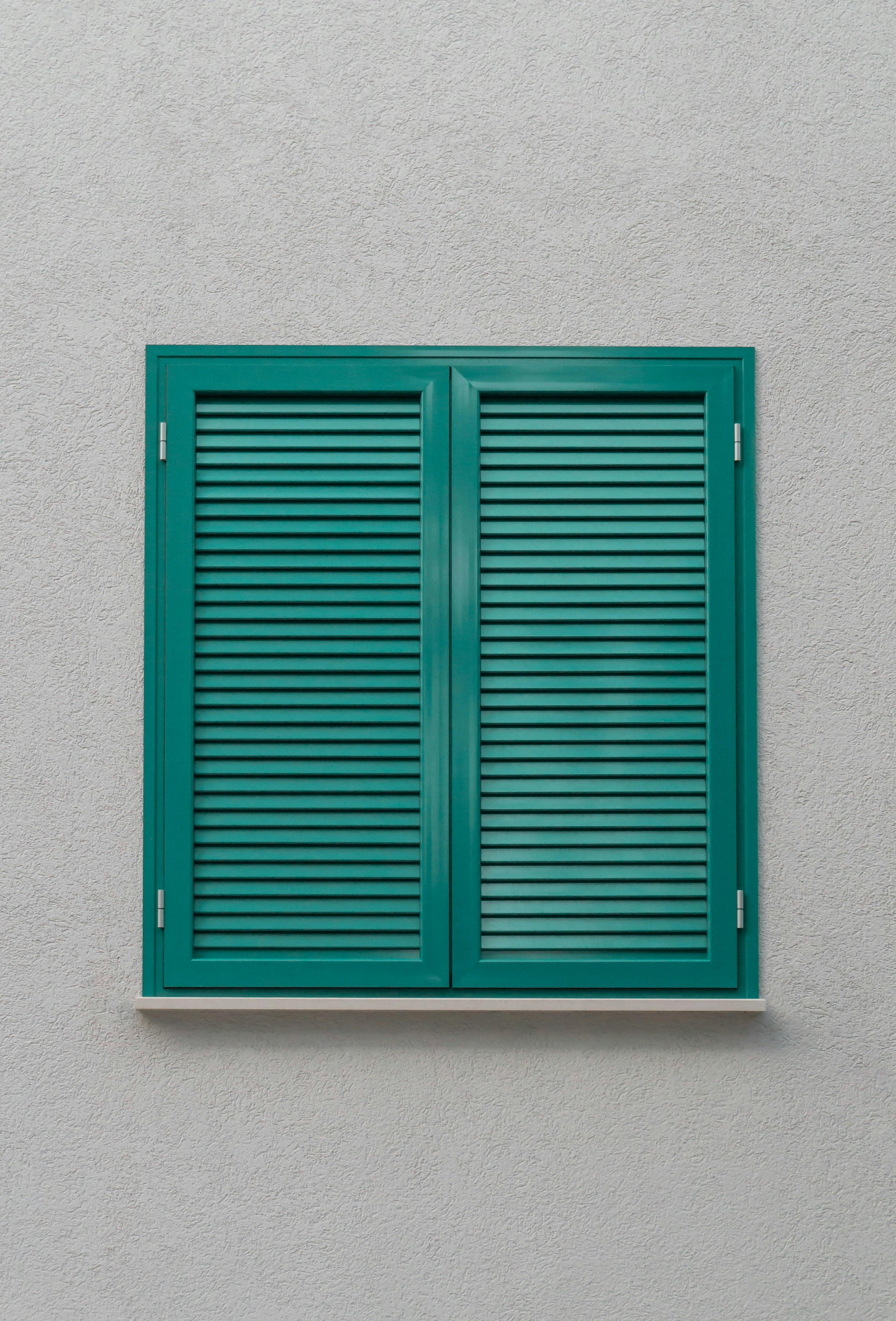 Simple green shuttered window on a textured white stucco wall with minimalist appeal.