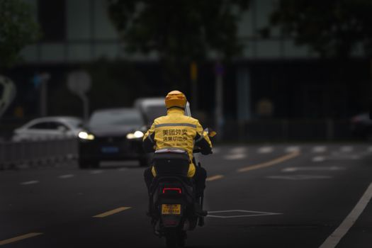 Urban delivery driver in yellow jacket on scooter navigating city streets.