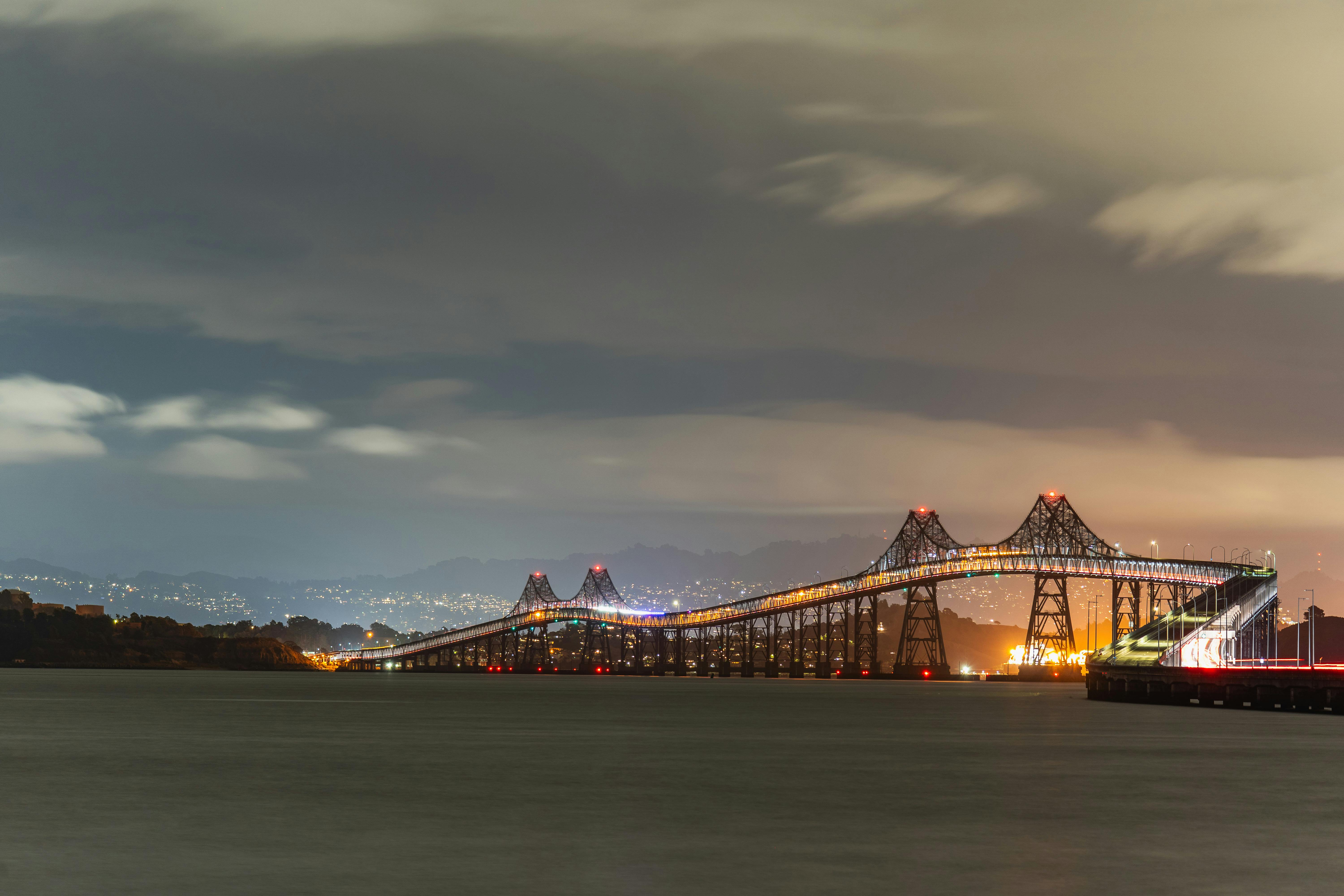 Illuminated Richmond-San Rafael Bridge over water at night with city lights in the background.