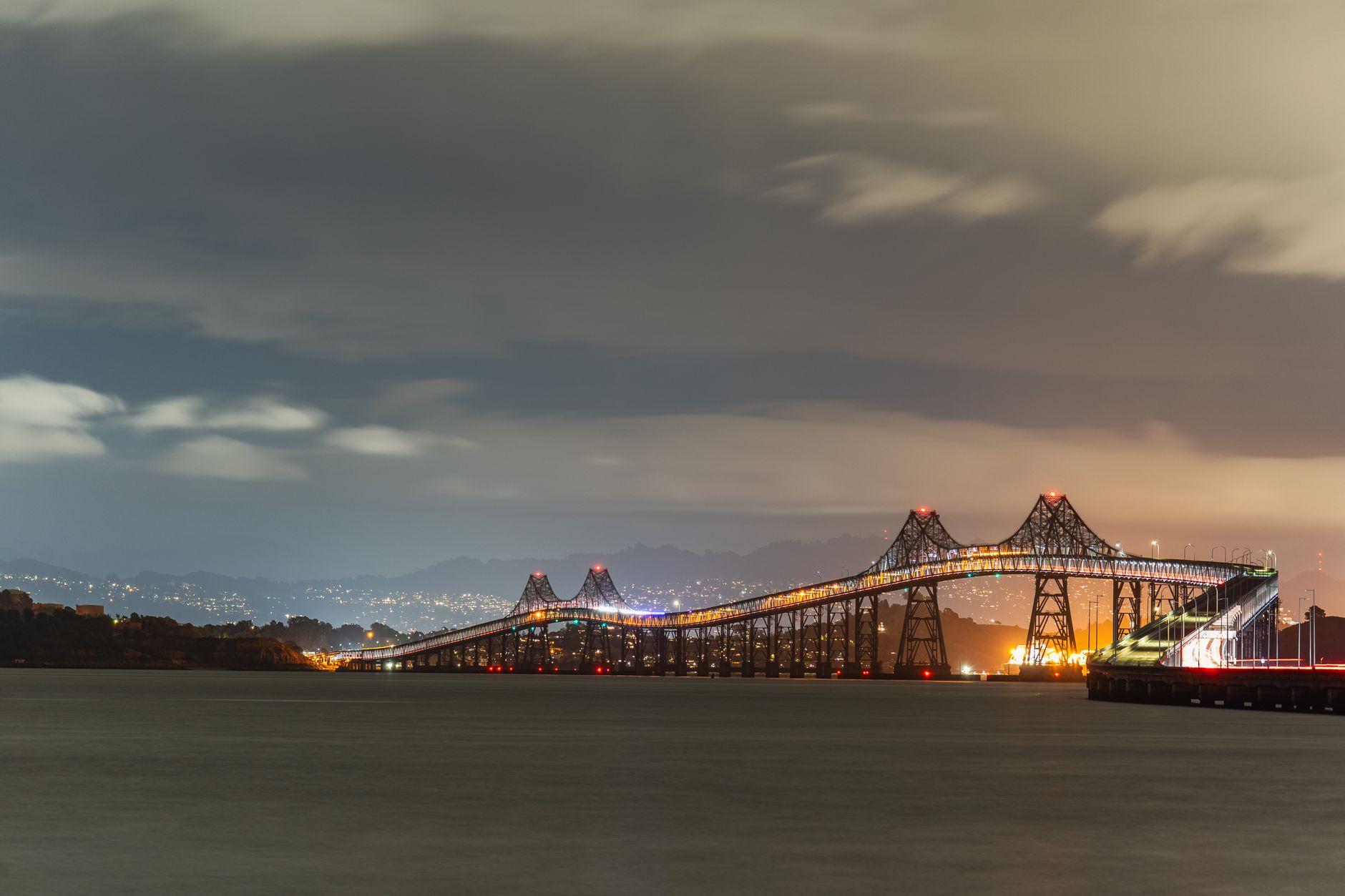 Illuminated Richmond-San Rafael Bridge over water at night with city lights in the background.