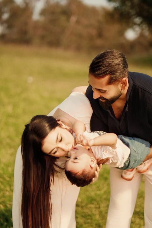 Free Joyful family bonding moment outdoors, parents playfully interacting with their child in a sunny park. Stock Photo
