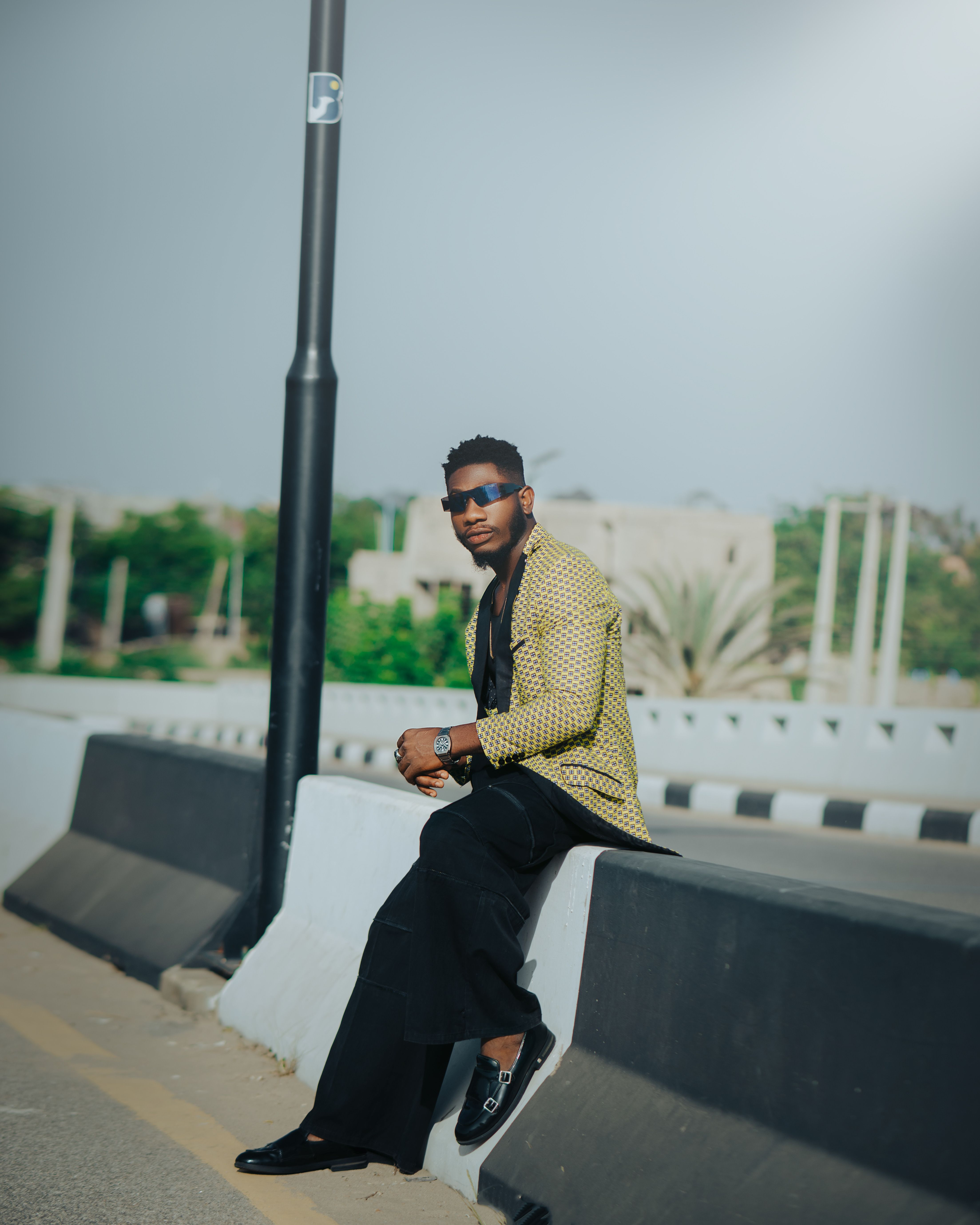 Fashionable man in sunglasses poses on a city street barrier in daylight.