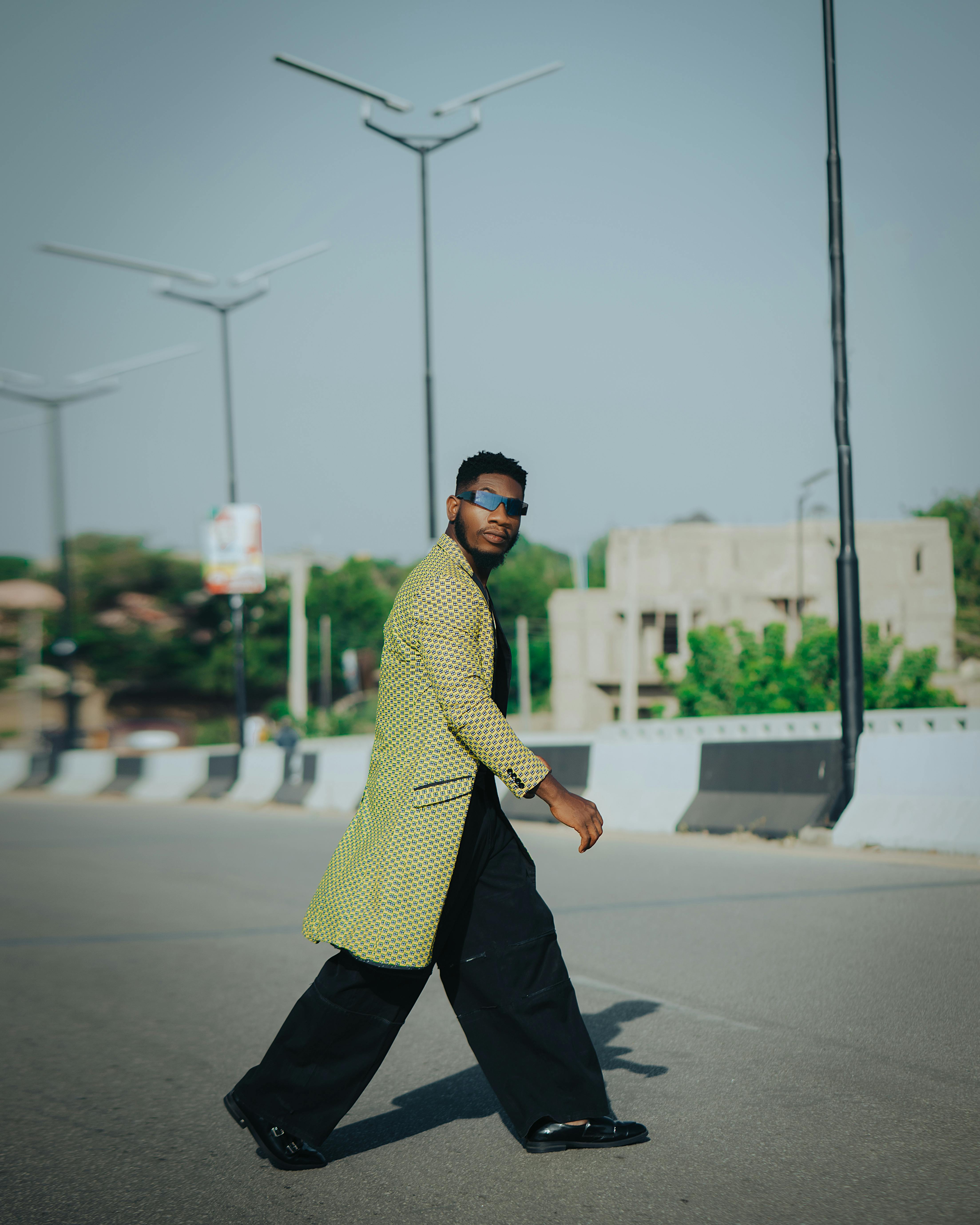 Fashionable man in sunglasses and coat crossing street, urban backdrop.