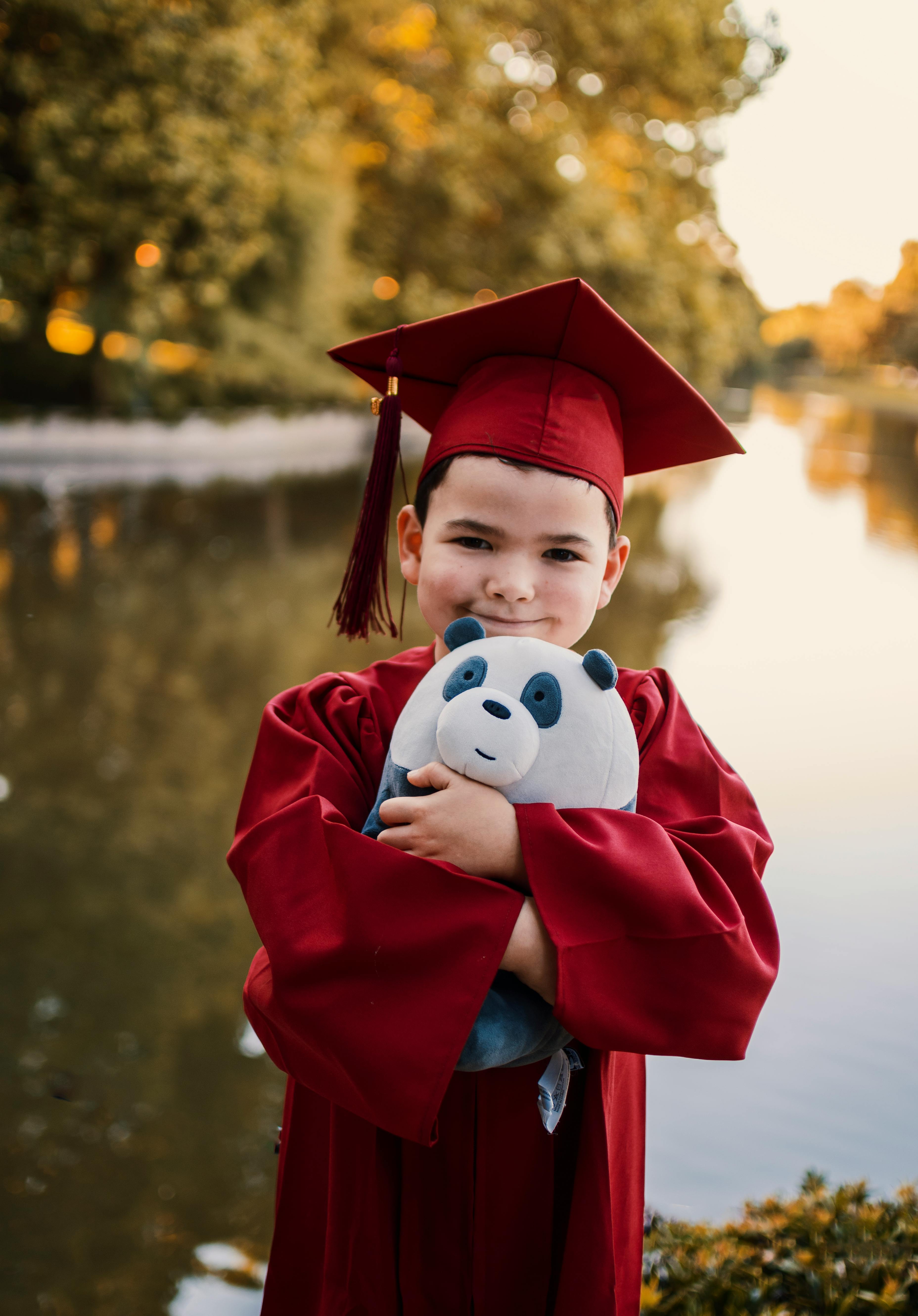 Young Graduate in Red Gown Holding Panda Toy Outdoors · Free Stock Photo