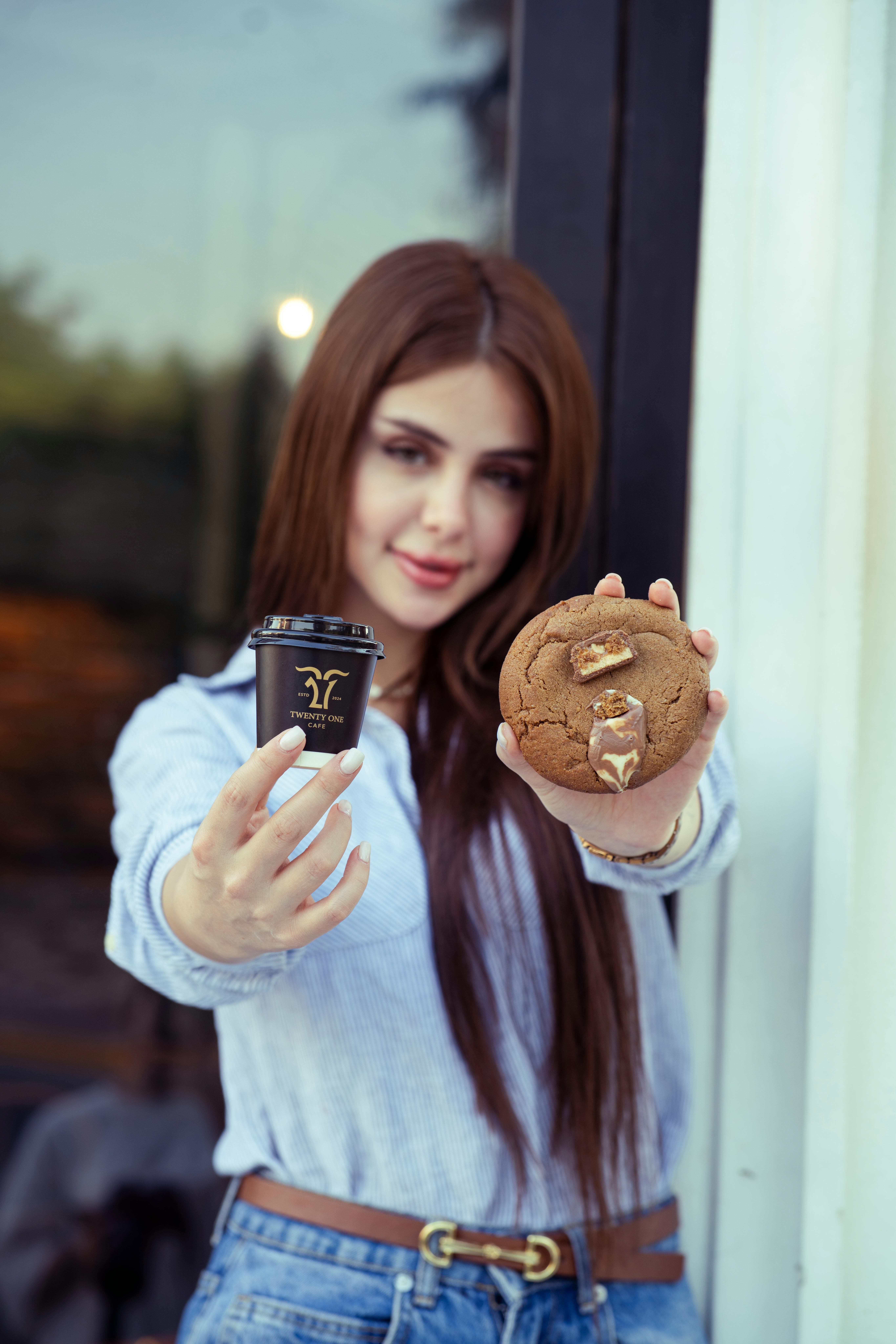 Miễn phí Một phụ nữ trẻ đang đưa tách cà phê và bánh quy bên ngoài một quán cà phê. Ảnh lưu trữ