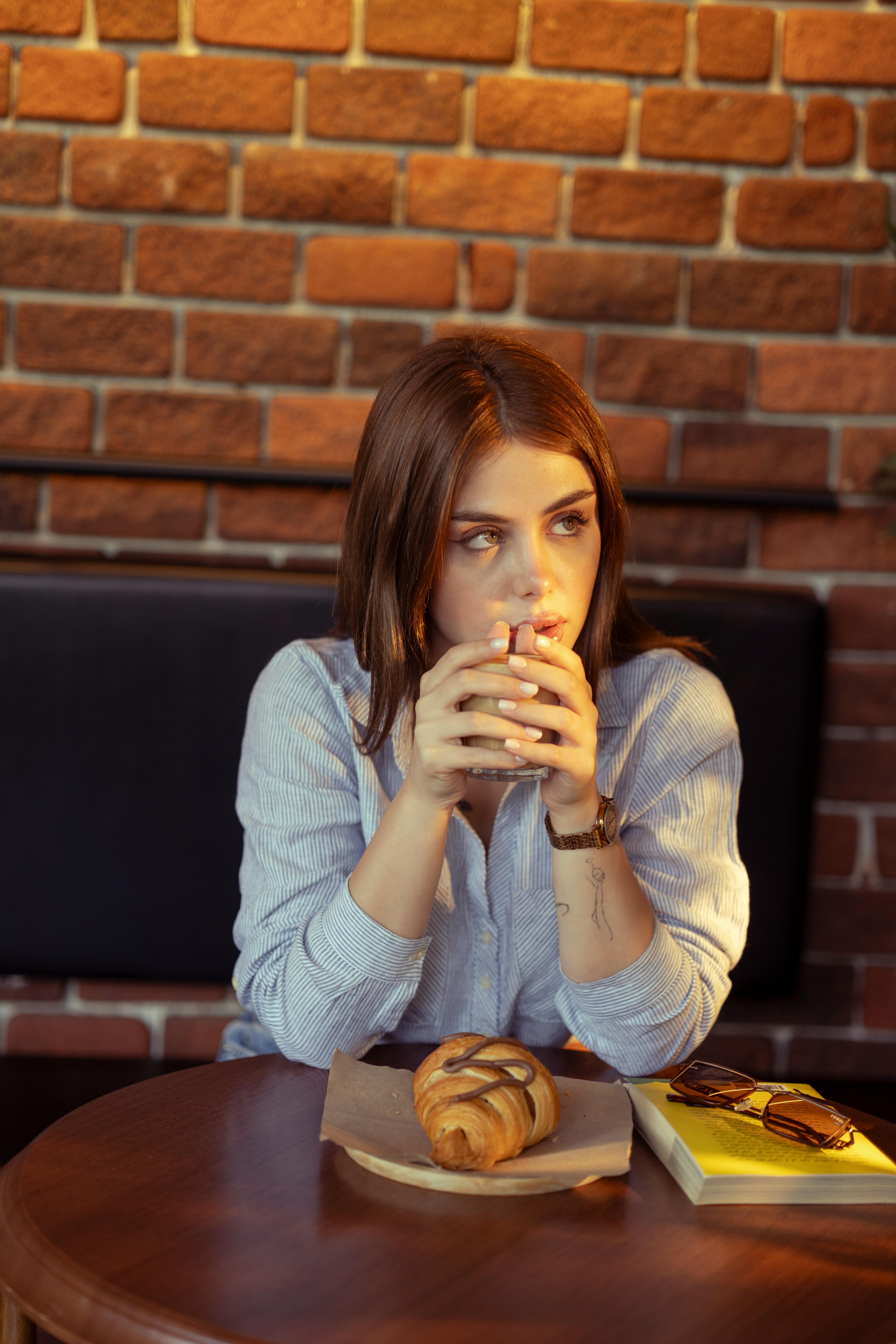 Kostenlos Eine Frau genießt in ungezwungener Atmosphäre ein heißes Getränk, auf dem Tisch liegen Gebäck und ein Buch. Stock-Foto
