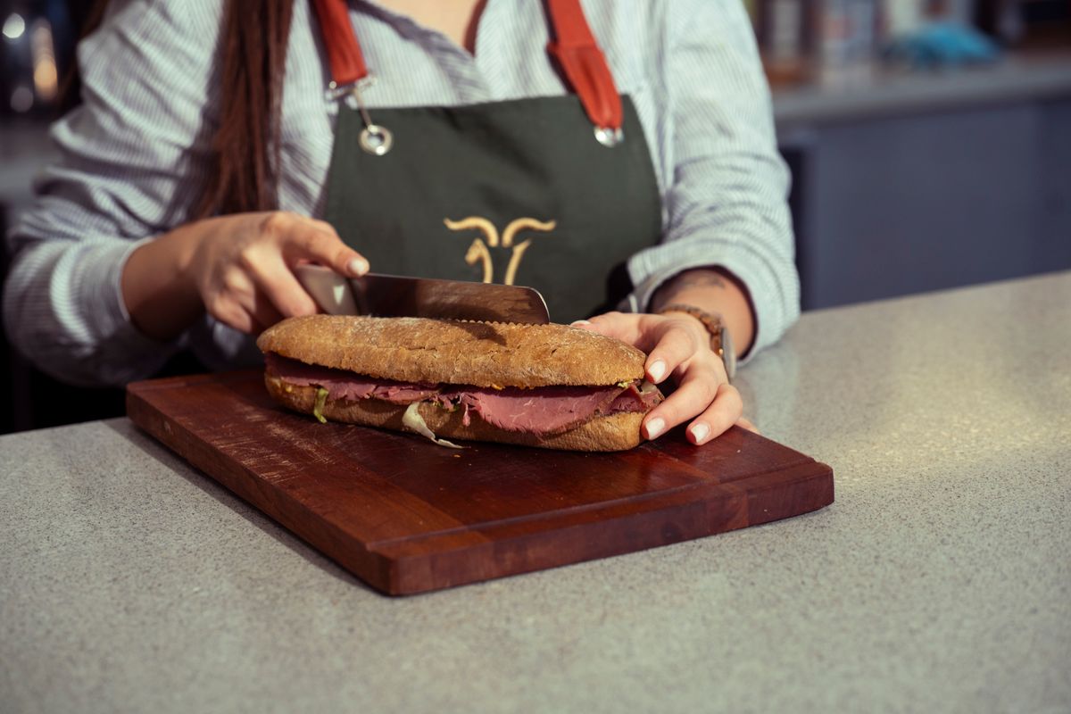 A cook slicing a fresh sandwich on a wooden board.
