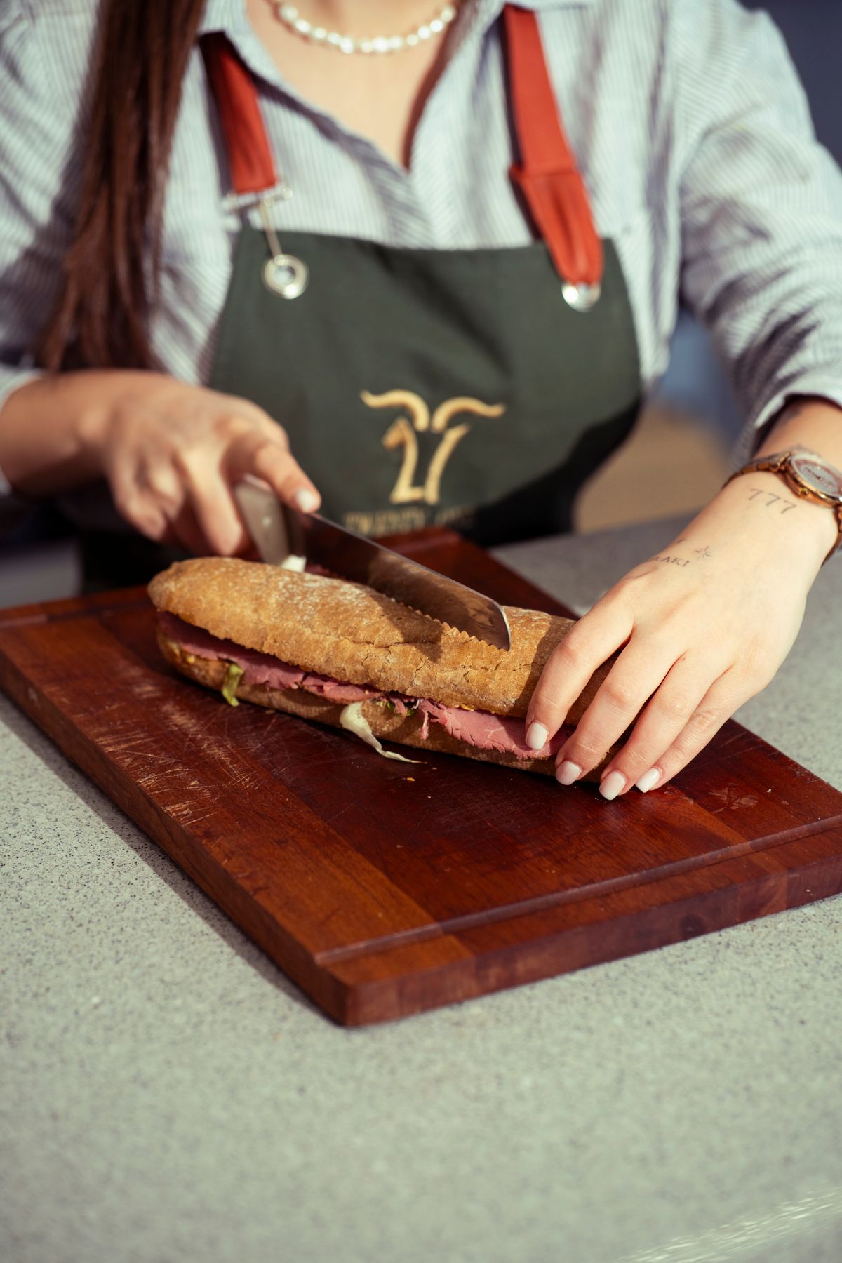 A chef slicing a fresh baguette sandwich on a wooden board