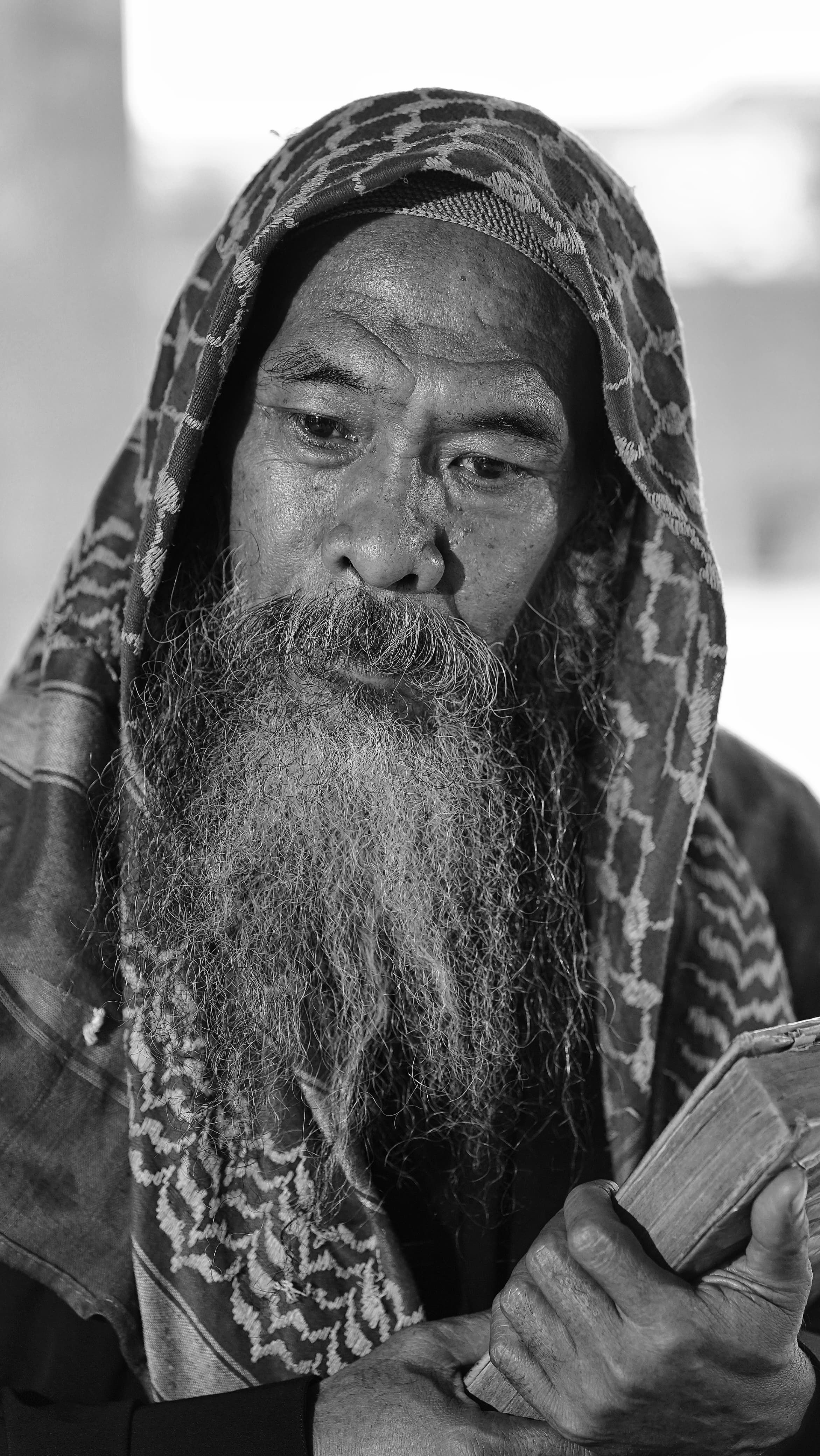 Black and white portrait of an elderly man with a beard holding a book, wearing traditional clothing.