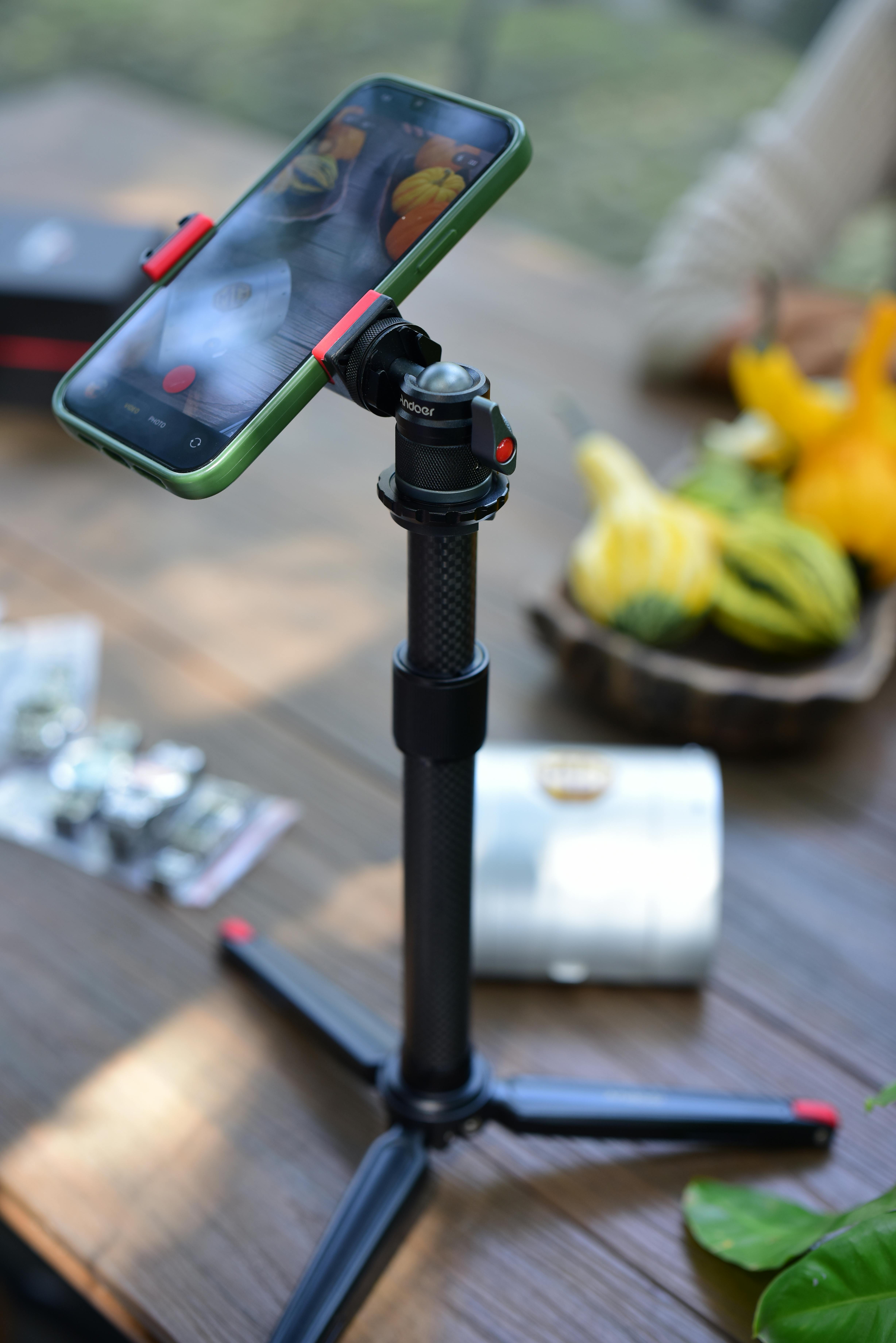 Free Smartphone mounted on a tripod with a colorful fruit setup in the background. Stock Photo