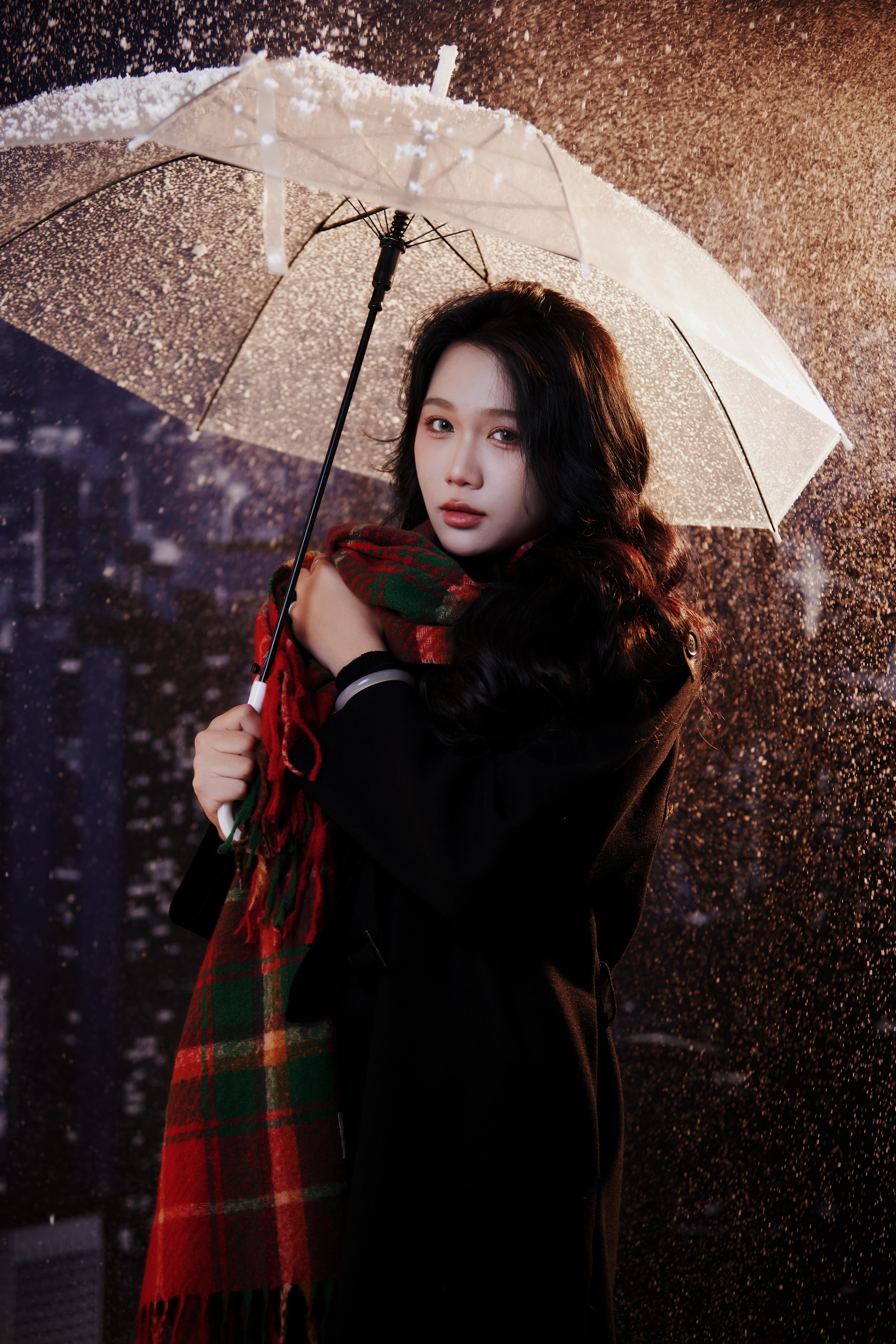 Young woman stands under umbrella during a rainy night, draped in a colorful scarf.