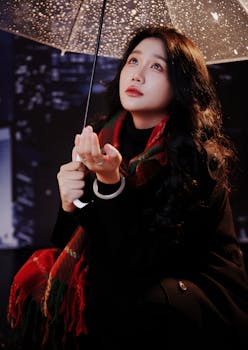 Woman in a coat and scarf under an umbrella at night, capturing a contemplative moment.