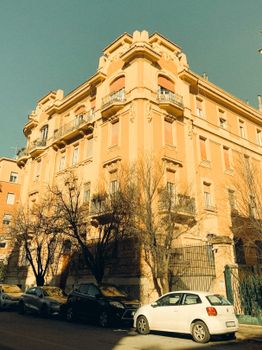 Vintage-style photograph of historical European architecture, bathed in warm sunlight with parked cars.