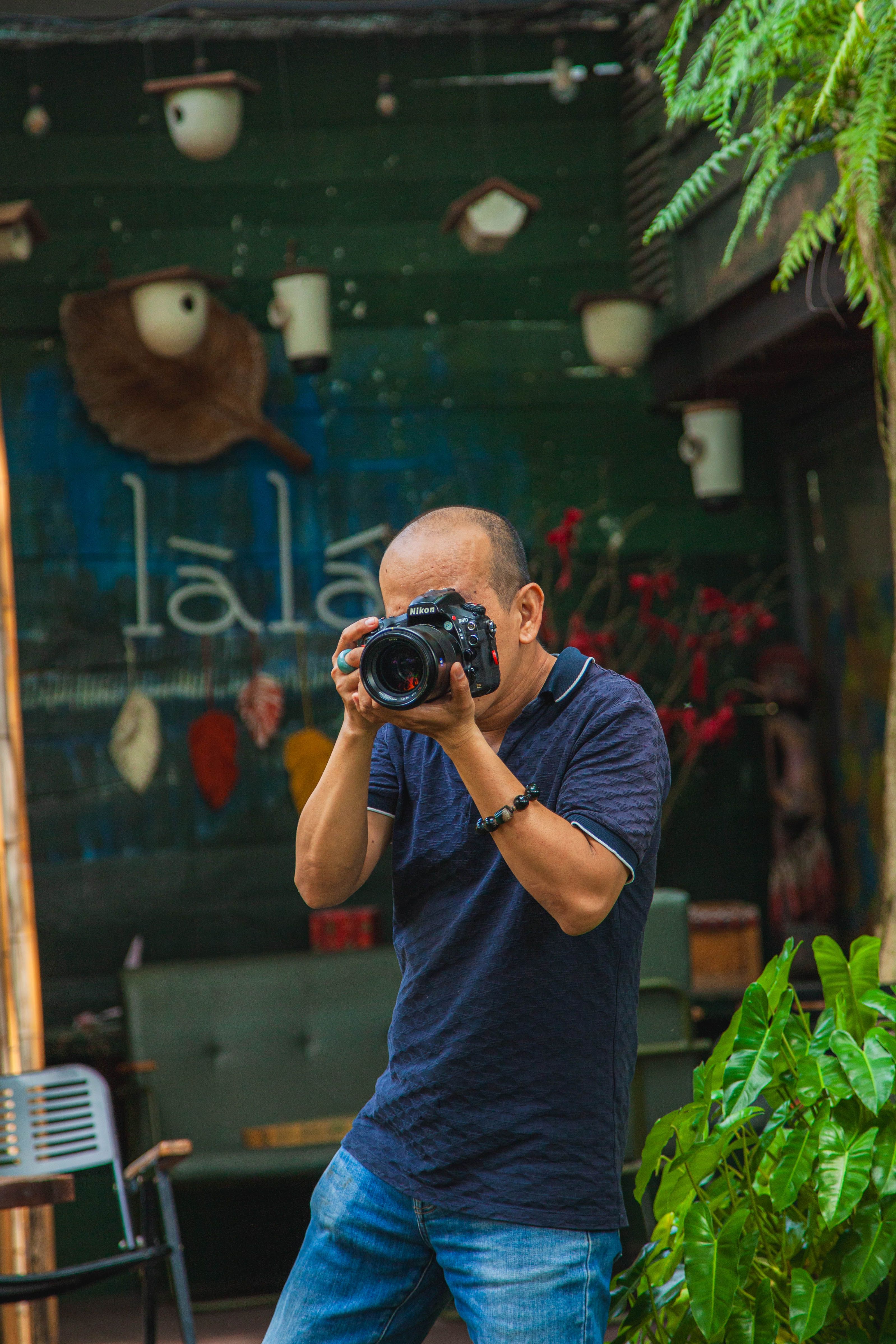 Male photographer takes a shot in an artistic café with greenery.
