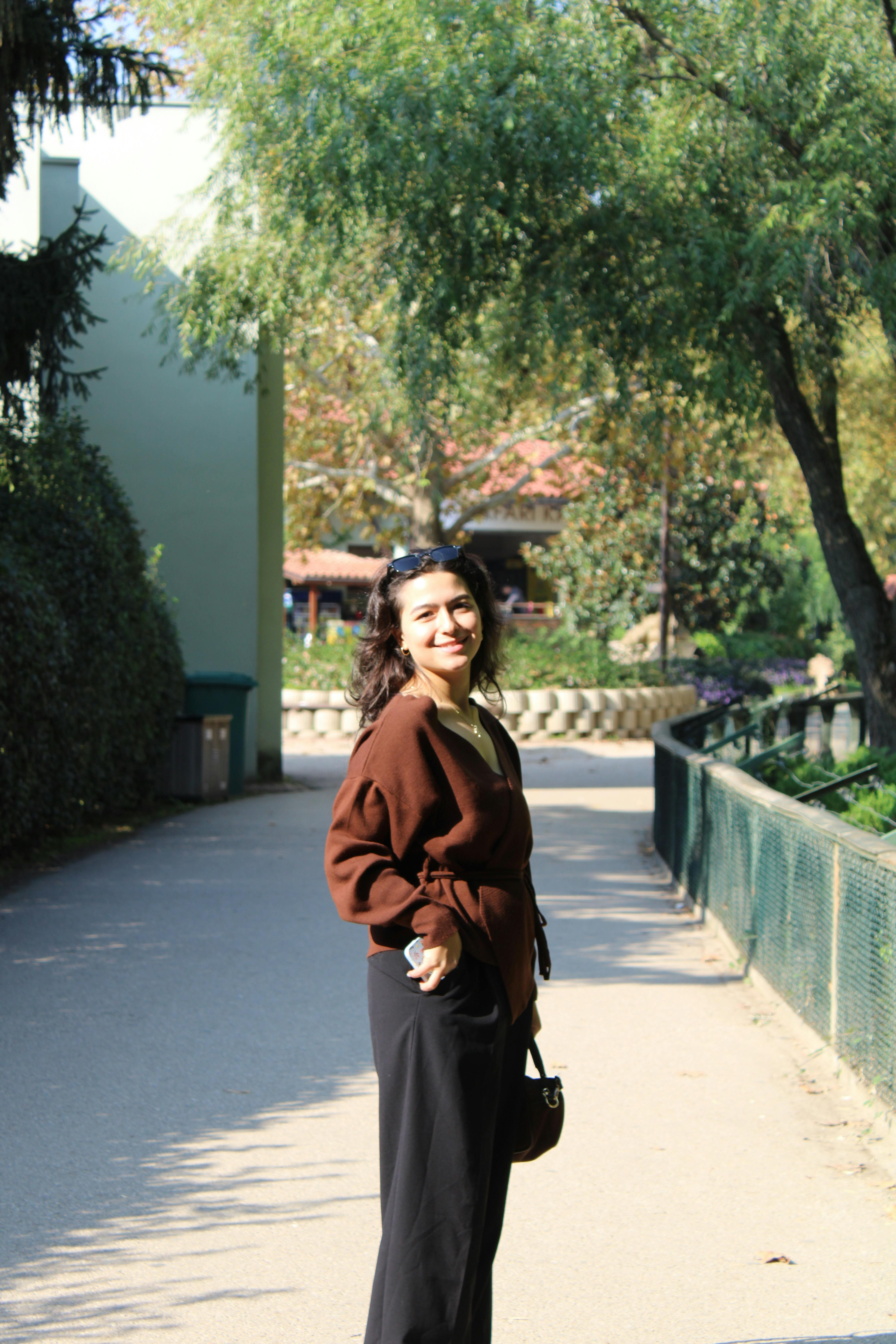 Smiling woman in a brown sweater enjoying a sunny walk outside.