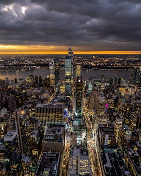 Aerial view of New York City's vibrant skyline during dusk with dramatic clouds and city lights.