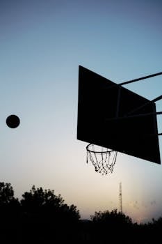 A basketball hoop and ball silhouetted against a twilight sky, perfect for sports themes.
