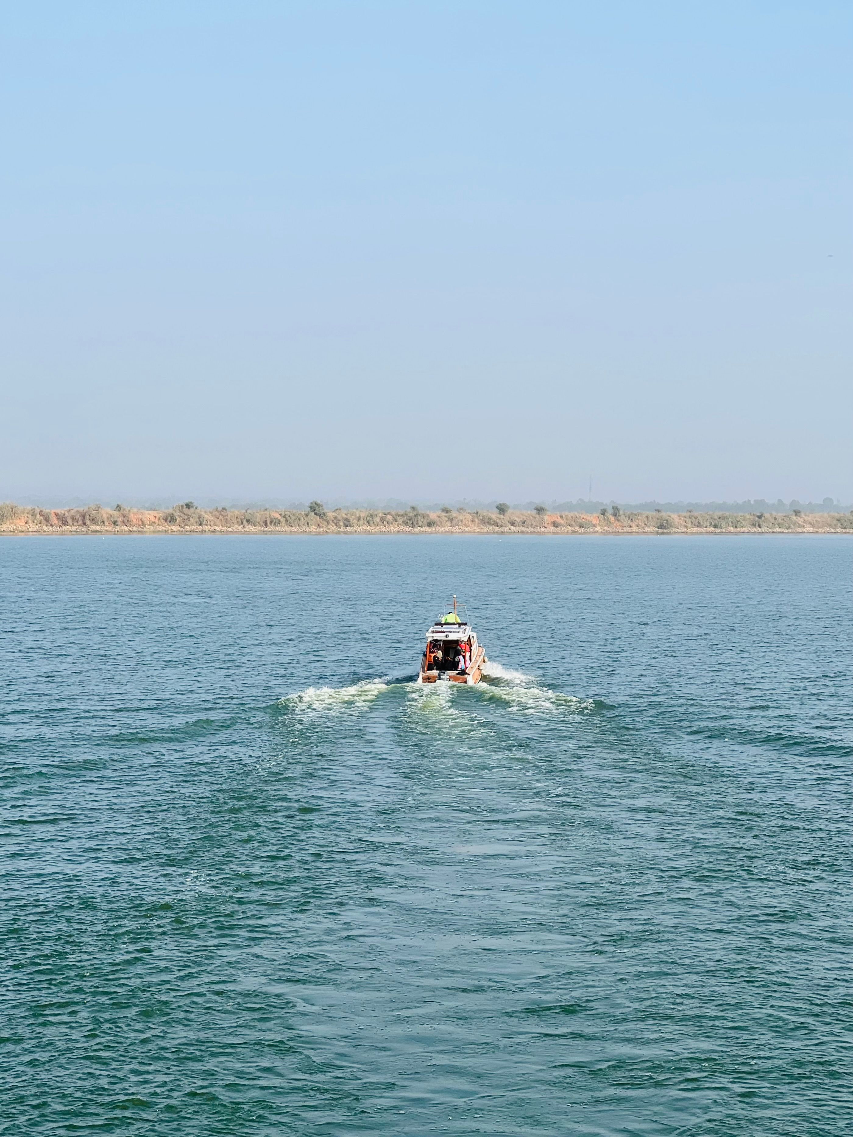 A speedboat gliding across a calm lake with clear blue skies in the background.