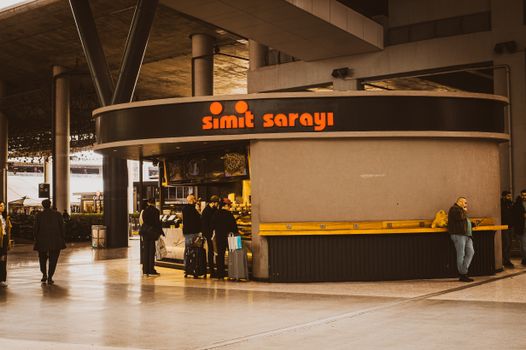 Travelers gather at a Simit Sarayı kiosk in a contemporary terminal setting, creating a lively atmosphere.